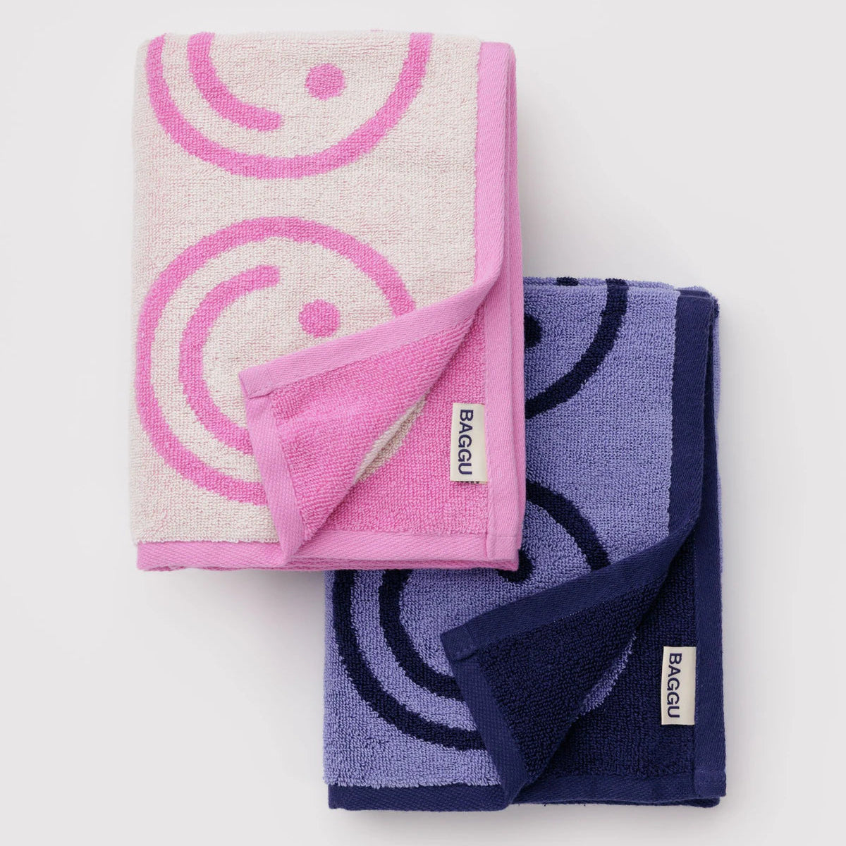 Two folded towels, one pink and one purple, with a smiley face patterned design