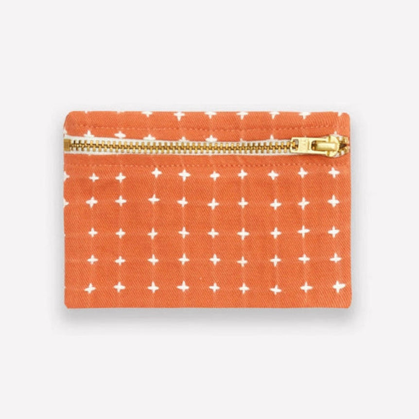 Small orange coin purse with white cross stitch pattern and gold zipper on a light gray background