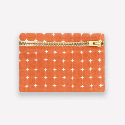 Small orange coin purse with white cross stitch pattern and gold zipper on a light gray background