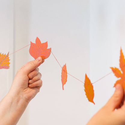 Person holding a string of orange paper leaves in front of a painting