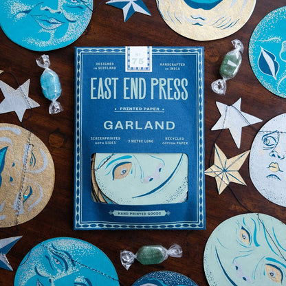 Pack of East End Press Moon Garland on a wooden surface with decorative paper cutouts.