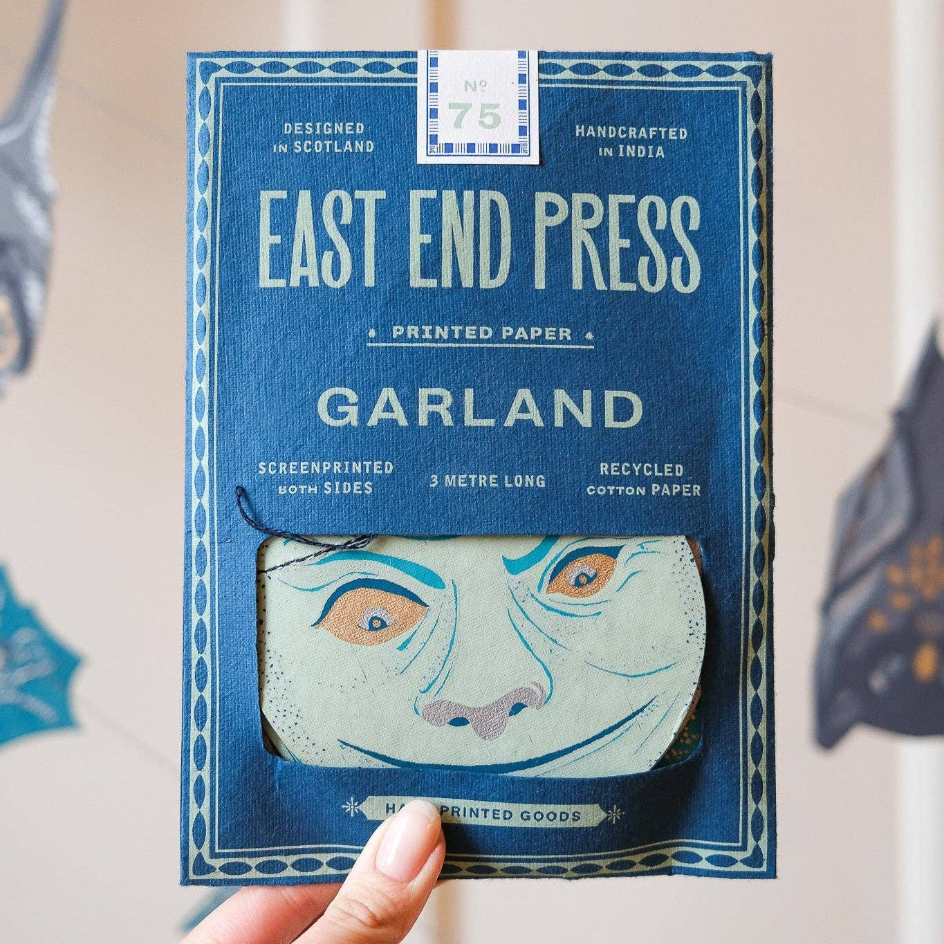 Hand holding a package of 'East End Press Garland' printed paper with a decorative moon design on a neutral background.