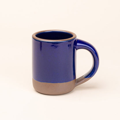 A ceramic mug with a glossy cobalt blue upper body and handle, and a contrasting matte brown glazed base
