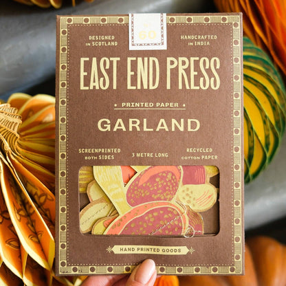 Handheld package of East End Press Mushroom Garland with pumpkins in the background
