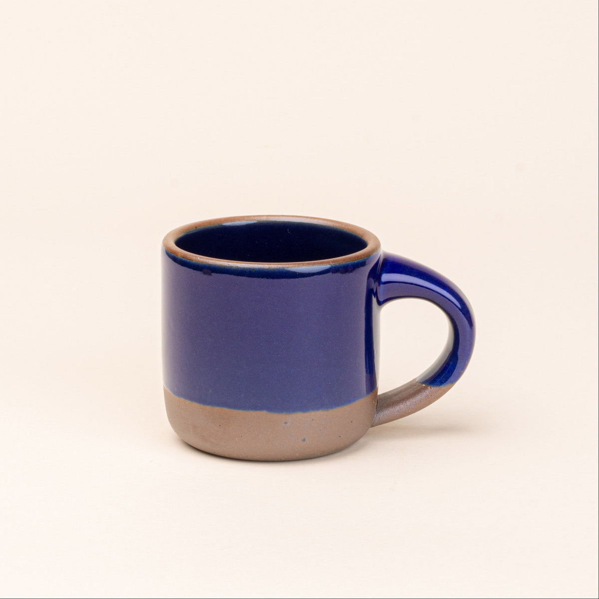 A small ceramic mug with a glossy dark cobalt blue upper body and handle, featuring a contrasting matte brown clay base and lip