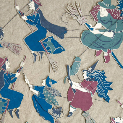 A close-up of a garland laid flat featuring multiple stylized witch figures in blue, teal, burgundy, and cream on a beige background.